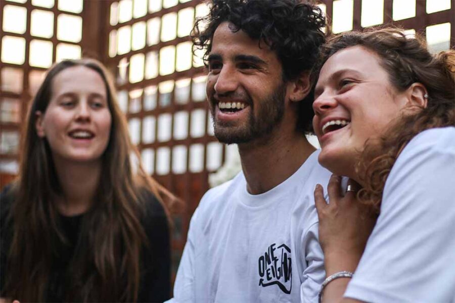 A young man wearing a white One Eighty t-shirt. There is a female on either site of him