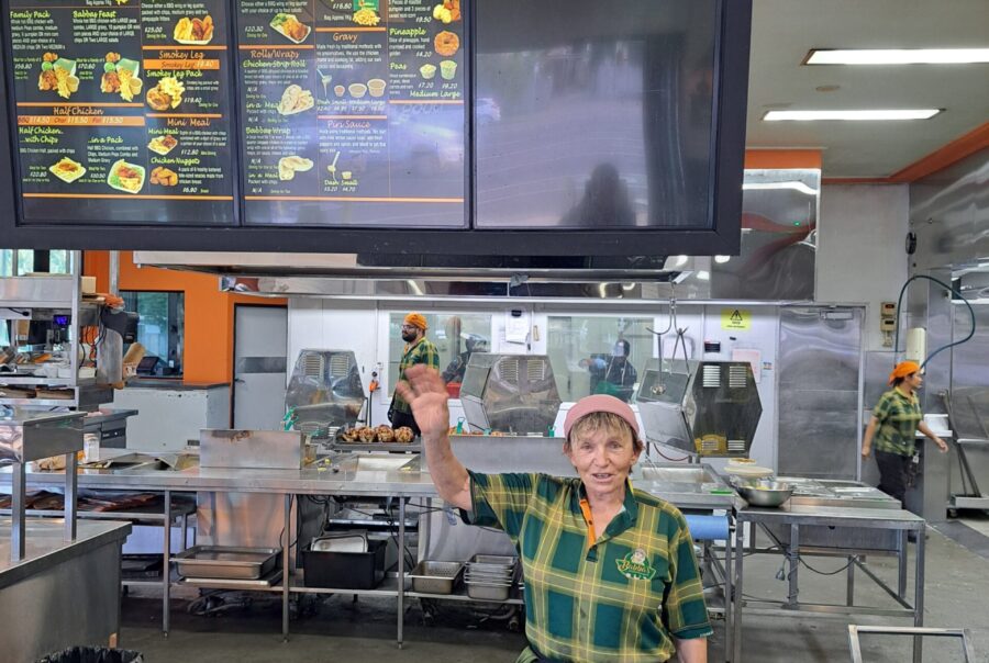 Nadia Softa smiling at the camera and pointing up at a menu on the wall above her.