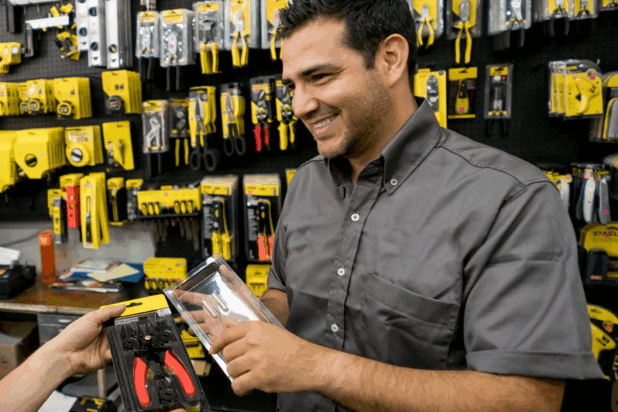Picture of a storeman smiling at a desk, behind him is rows of tools.