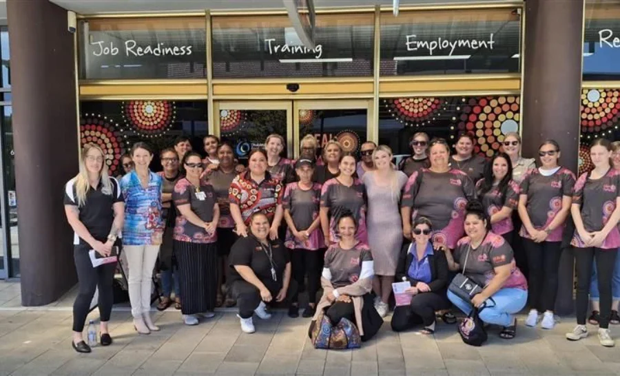 A group of women wearing indigenous patterned shirts stand in front of the gym where Her Futures Wellbeing Program takes place.