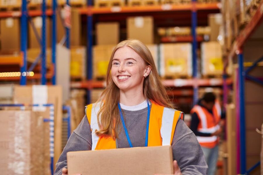 Young female wearing safety vest happily working in a warehouse