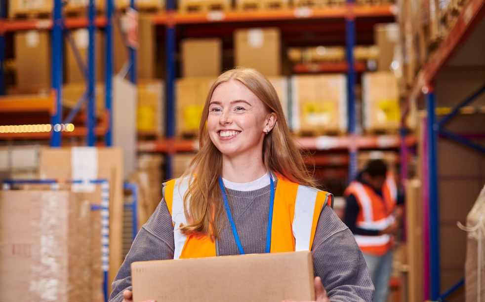 Young female wearing safety vest happily working in a warehouse