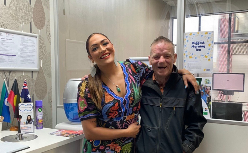 Tim smiling happily alongside his AKG job coach, Michele, who has her arm around his shoulder in a brightly lit office setting