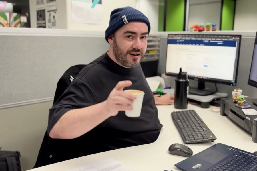 Man in a beanie holding a small takeaway coffee cup during a barista training session at a computer desk.