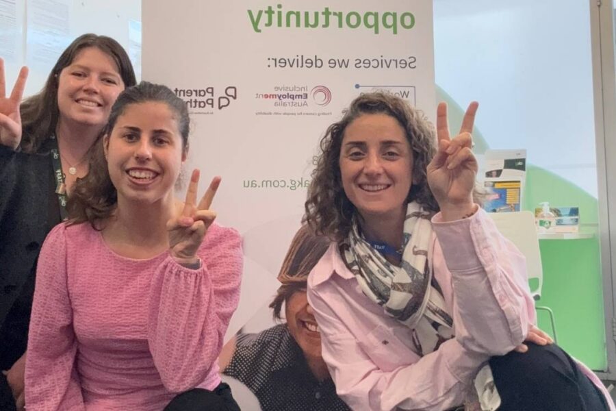 Catherine smiling alongside two AKG team members posing with peace signs in an office.