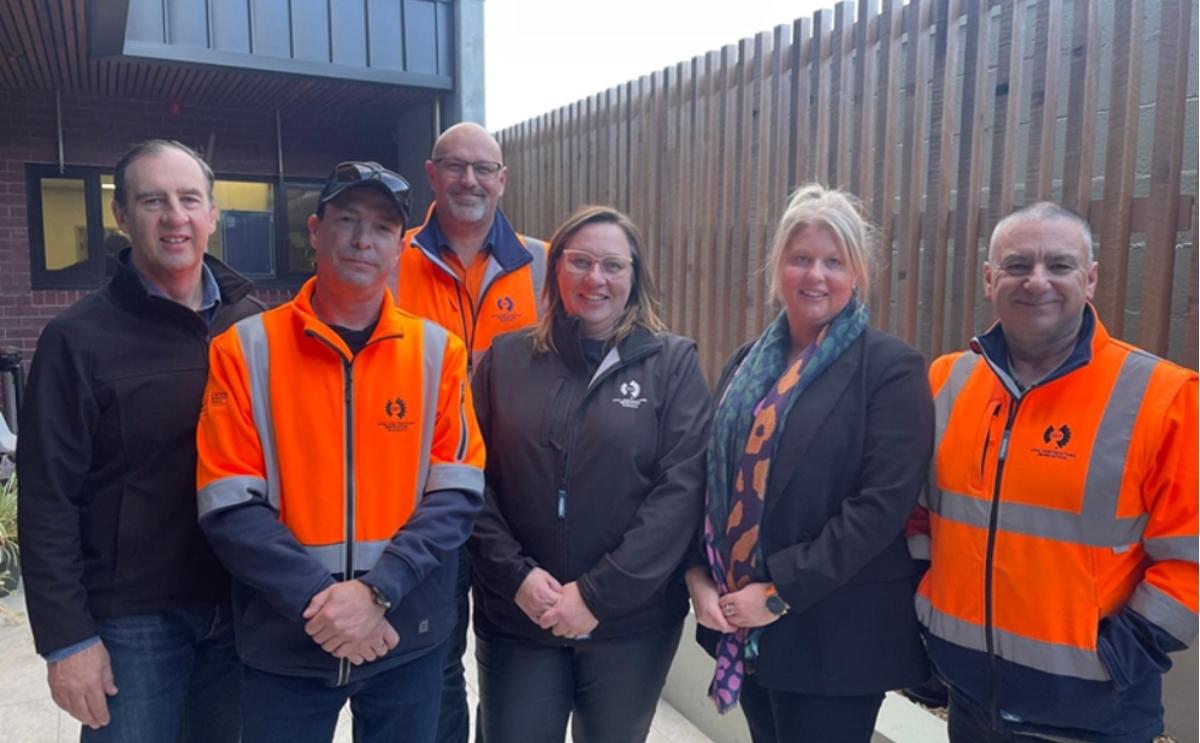 Representatives from AKG, Bethlehem House, and Vinnies Housing standing together outside, wearing high-visibility work jackets and smart casual clothing.