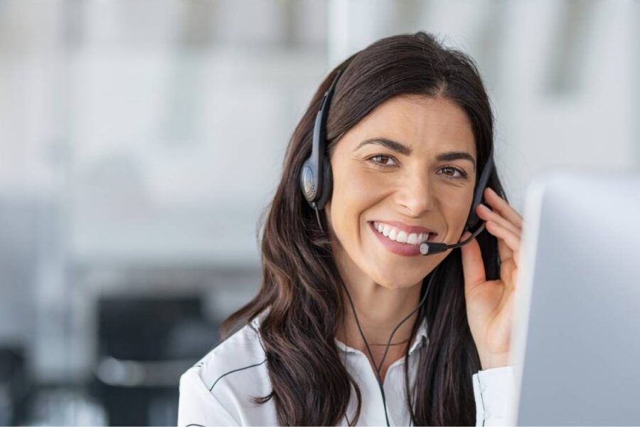 A smiling contact centre representative wearing a headset sitting at a computer workstation.