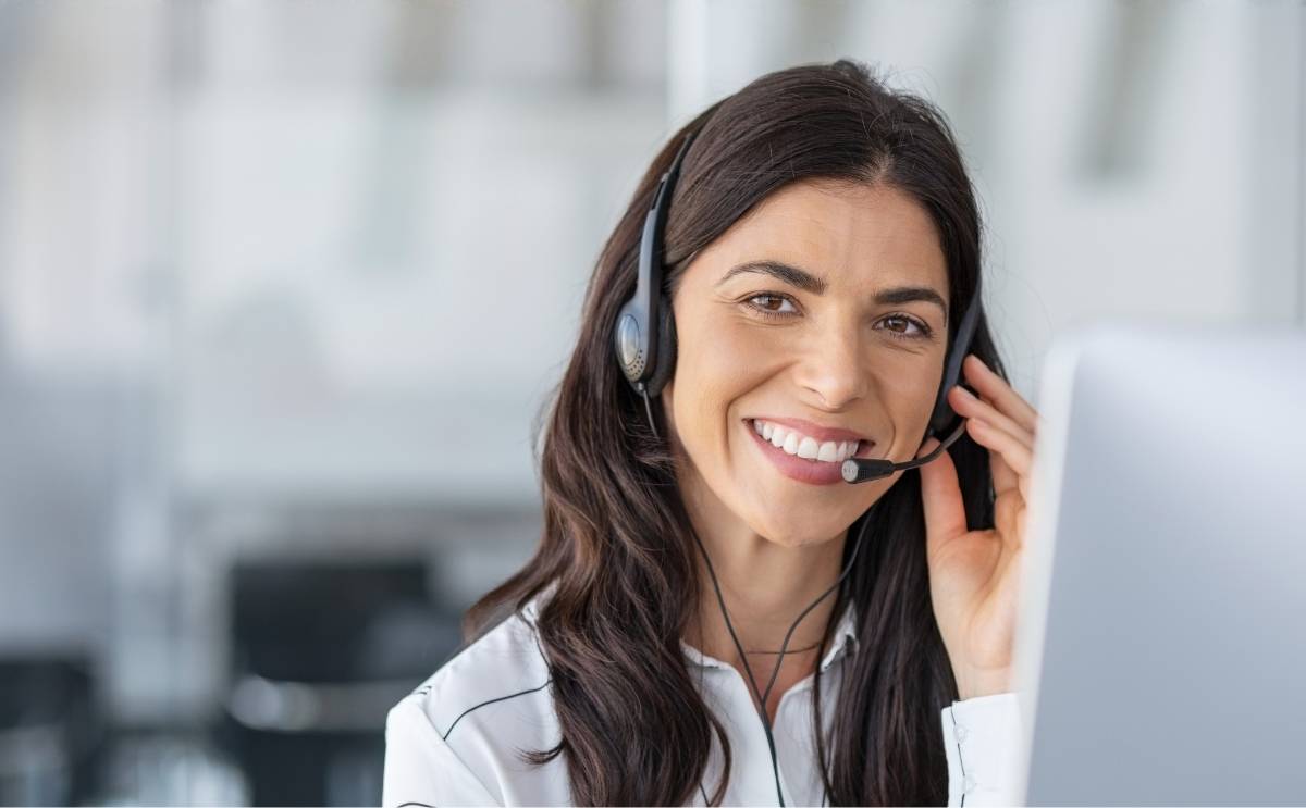 A smiling contact centre representative wearing a headset sitting at a computer workstation.