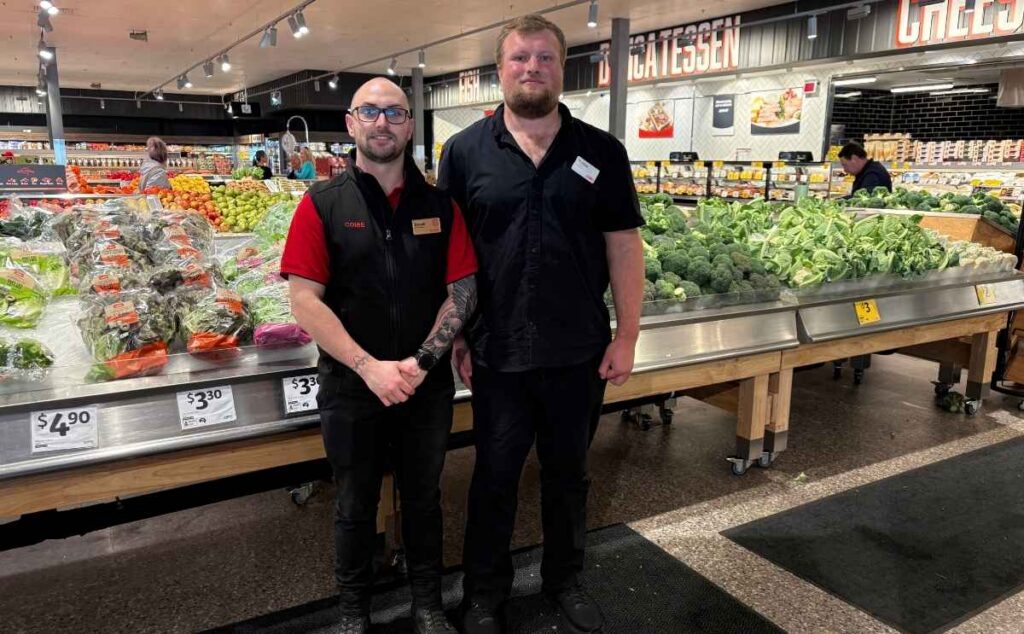 Coles store employee standing beside a colleague in the supermarket fresh produce section