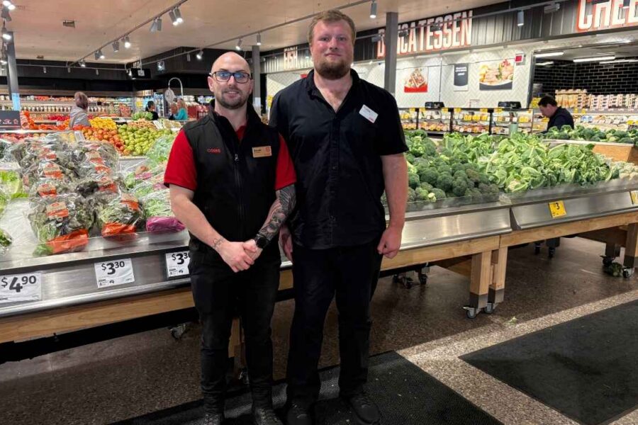 Coles store employee standing beside a colleague in the supermarket fresh produce section